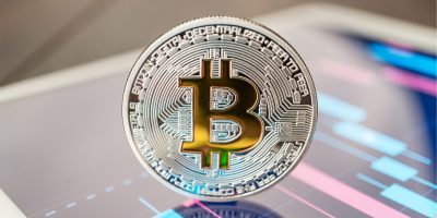 close-up photo of bitcoin cryptocurrency physical coin on the tablet computer showing stock market charts. trading bitcoin cryptocoin concept on the wooden table